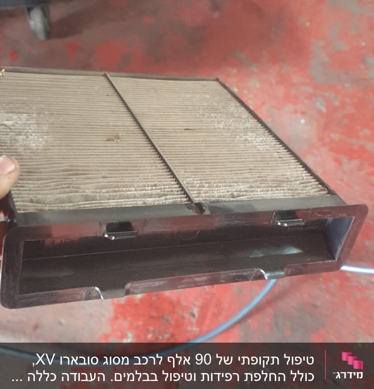 פילטר אוויר מלוכלך מוחזק ביד על רקע רצפה אדומה